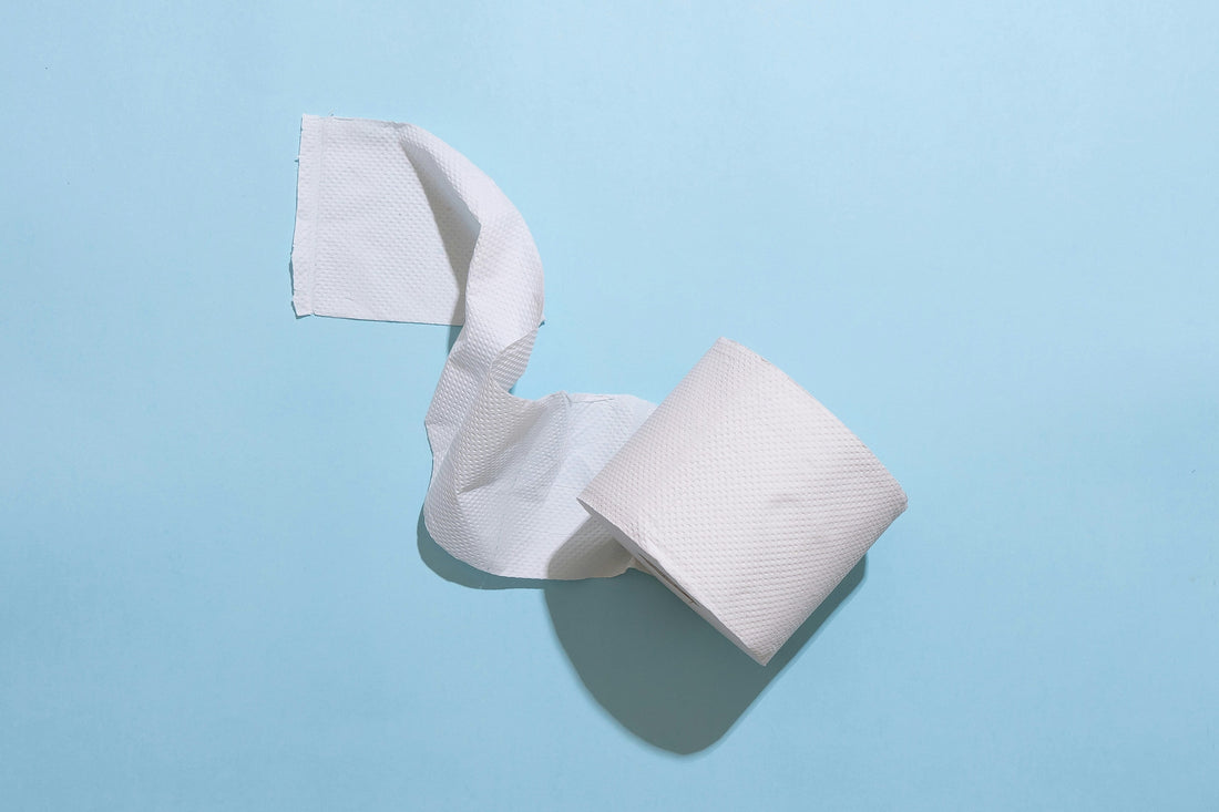 A roll of white toilet paper unspooling against a soft pale background.