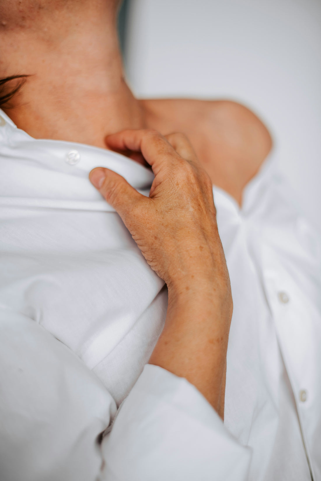 A woman in a white shirt rests her hand on her upper chest, a common gesture when noticing a racing or fluttering heartbeat.