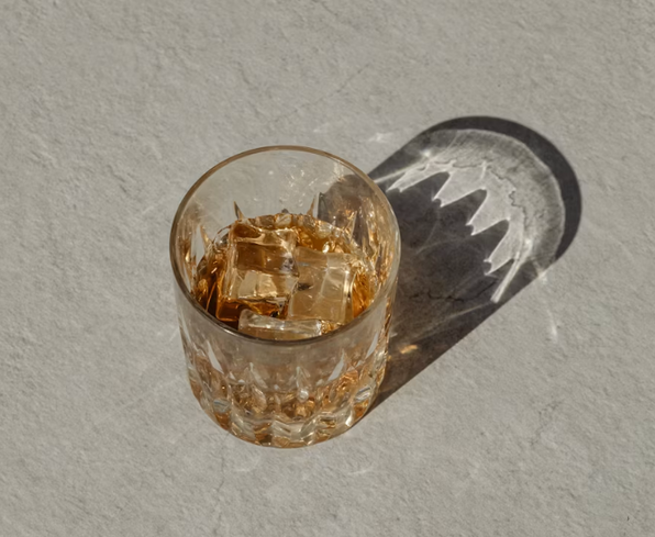A cut-crystal glass of whisky on ice casting a long shadow across a pale neutral surface.