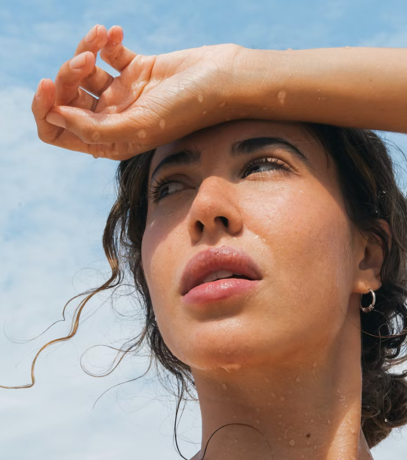 Woman wiping her brow during a hot flush, standing outdoors against a blue sky