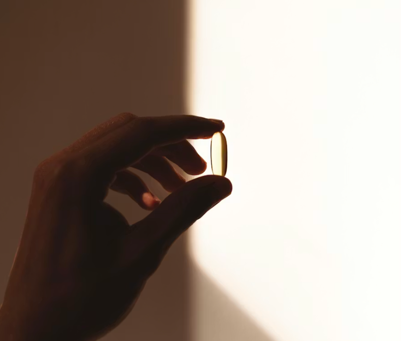 Silhouette of a hand holding a soft-gel supplement capsule in warm light