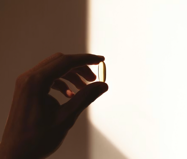 Silhouette of a hand holding a soft-gel supplement capsule in warm light